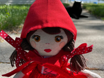 My Little Red doll sitting on a sidewalk with a black kitty in the background.