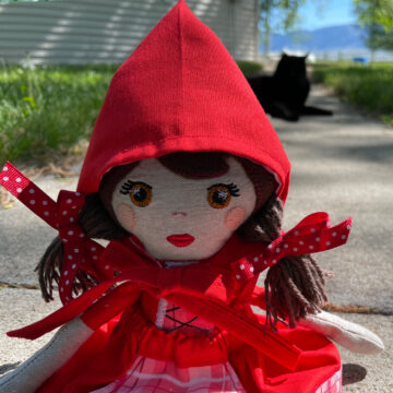 My Little Red doll sitting on a sidewalk with a black kitty in the background.