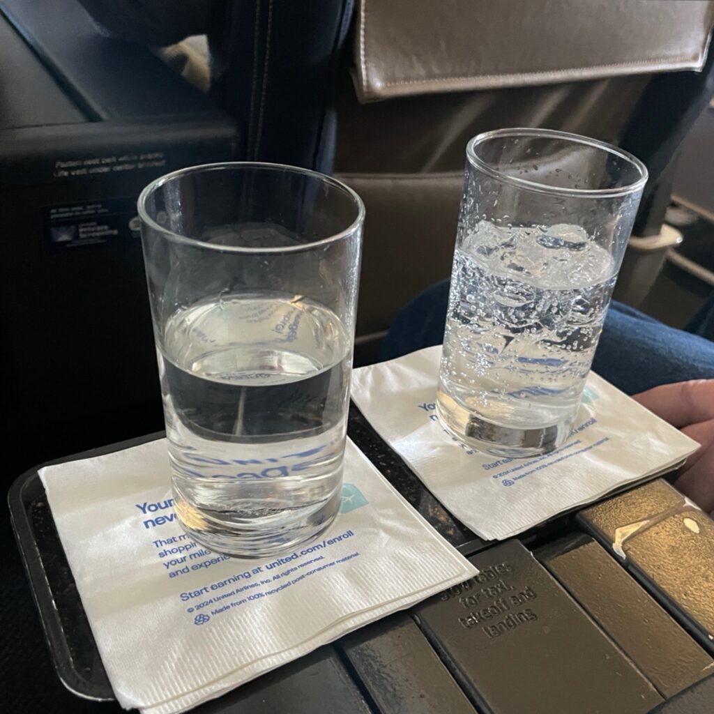 A glass of water and a glass of Sprite place on napkins on the tray table between our seats. 