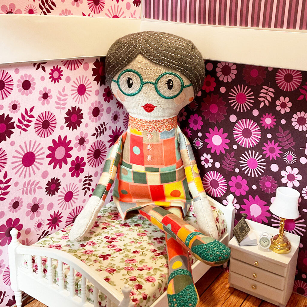 The Grandma doll is sitting on the little bed in my dollhouse. 