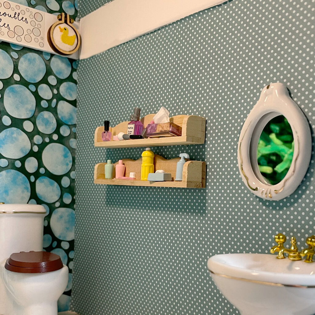 My dollhouse bathroom with two shelves of beauty supplies, a mirror, a sink, and a toilet. 