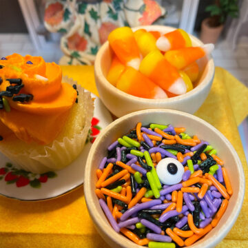 A cupcake on a plate, a mini bowl of candy corn, and a mini bowl of candy worms and an eyeball.