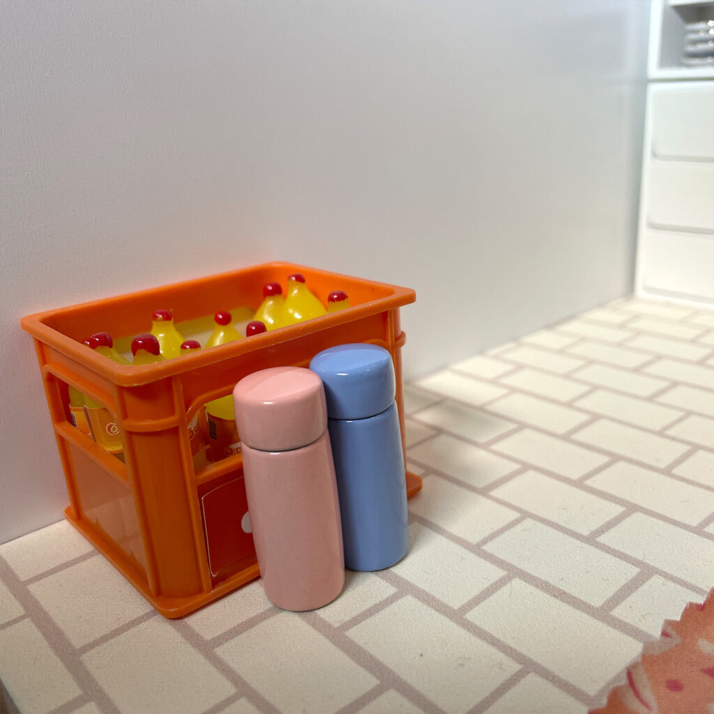 A mini crate with bottles of orange pop and two metal water bottles with lids in front. 