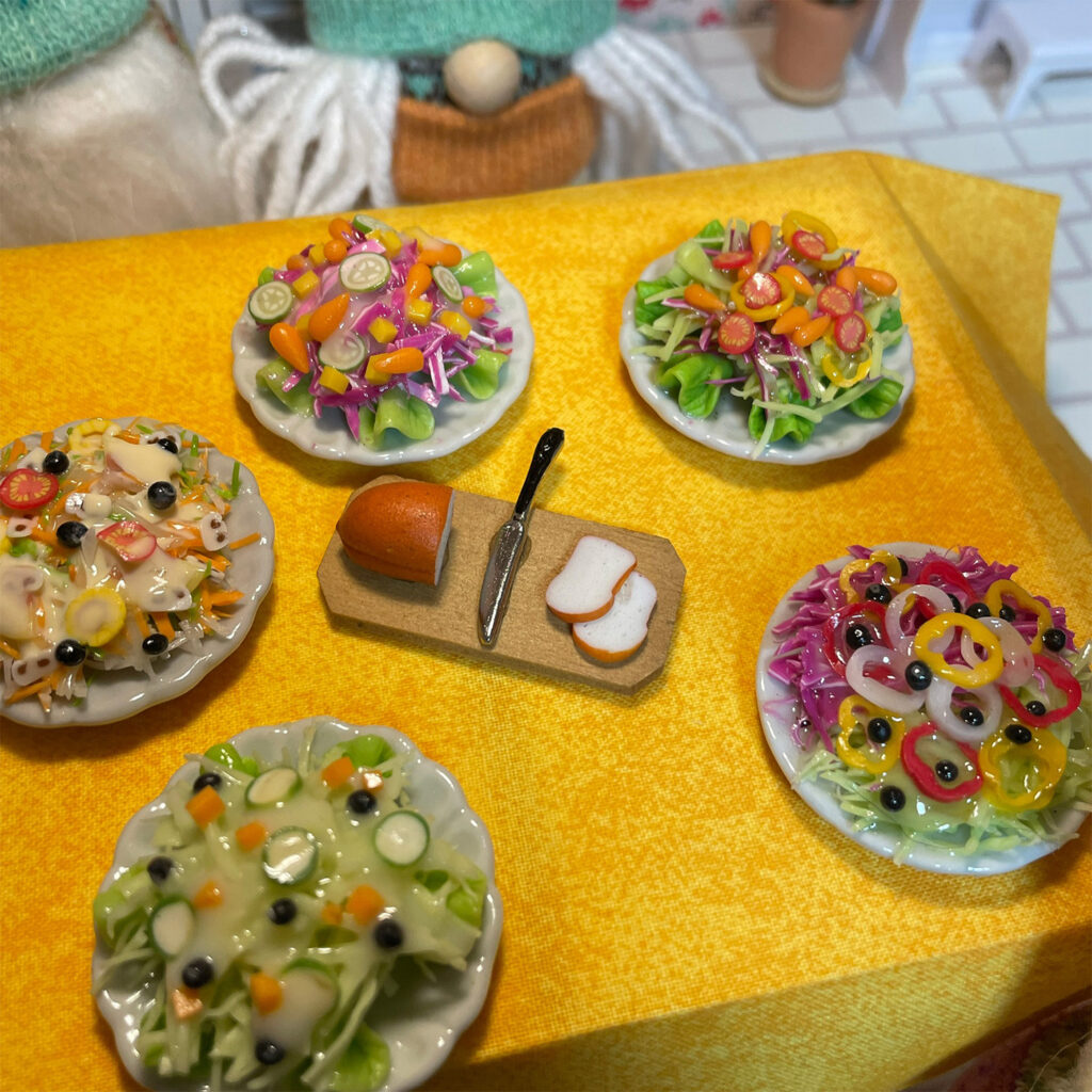 A table laden with mini plates of salads and a breadboard with bread, a knife, and bread slices on it. 