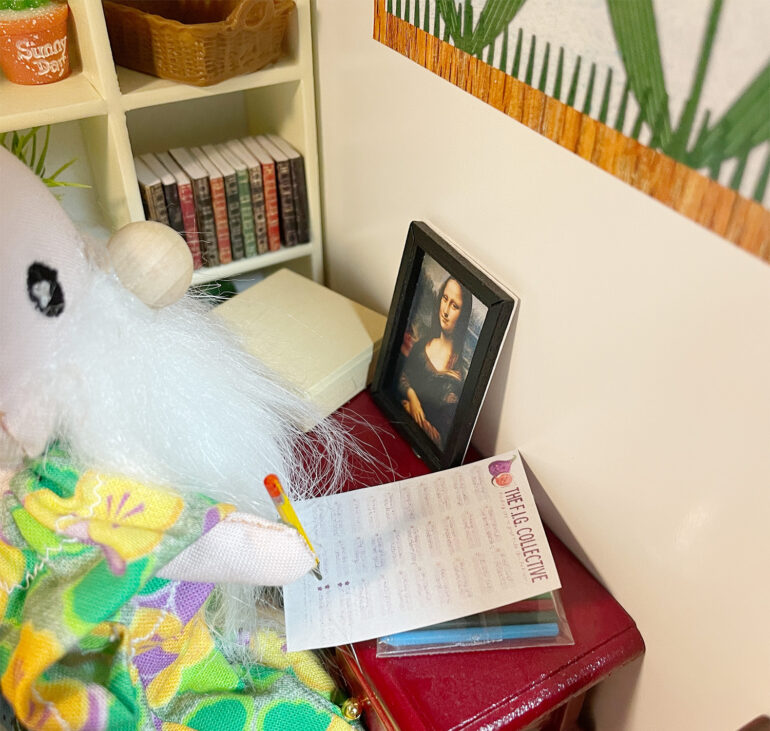 A little doll with a beard and a bead nose is sitting at a desk writing on a piece of paper.